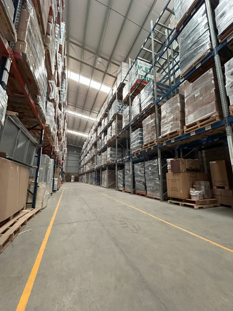 Bodega de almacenamiento en seco con racks azules y rojos con pallets, cajas de cartón y muebles envueltos en plástico transparente. Almacenamiento Guadalajara