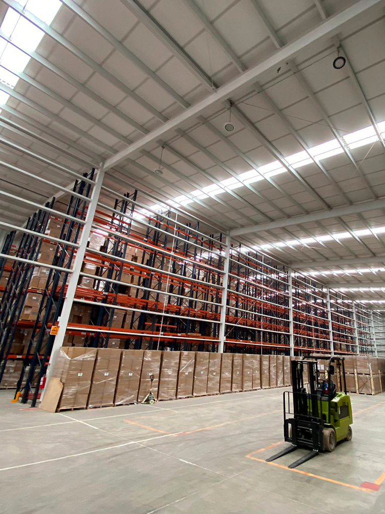 Bodega de almacenamiento en seco con racks vacíos, un montacargas y cajas de cartón apiladas encima de pallets Almacenamiento Guadalajara