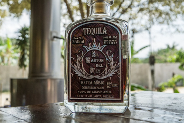 botella de tequila sobre una mesa de madera y fondo de plantas Almacén Guadalajara