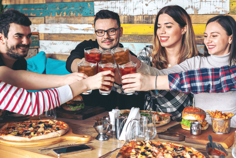Grupo de amigos brindando con aguas de sabor sentados en una mesa con mucha comida Almacén Guadalajara